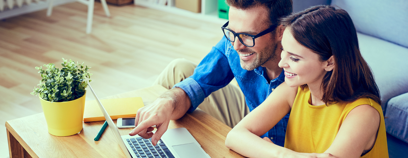 Couple sitting on floor with laptop computer.